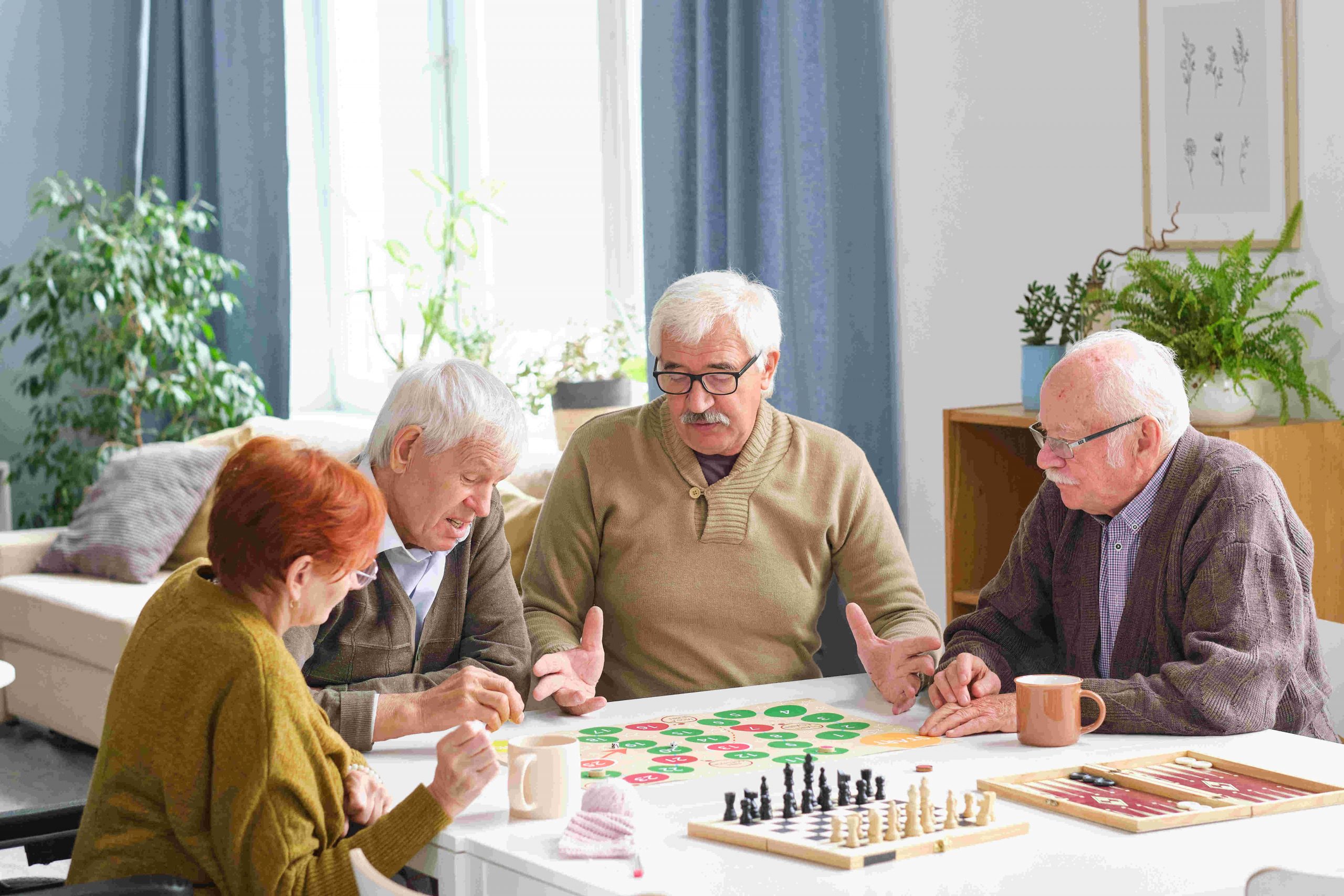 Group of elderly people sitting at the table and playing board game in the room